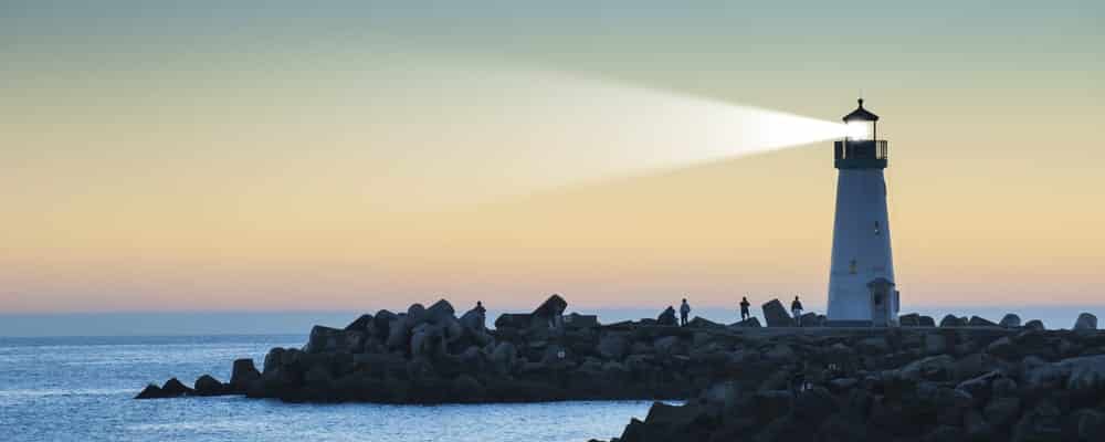 Lighthouse-emitting-beam-of-light-at-sunset