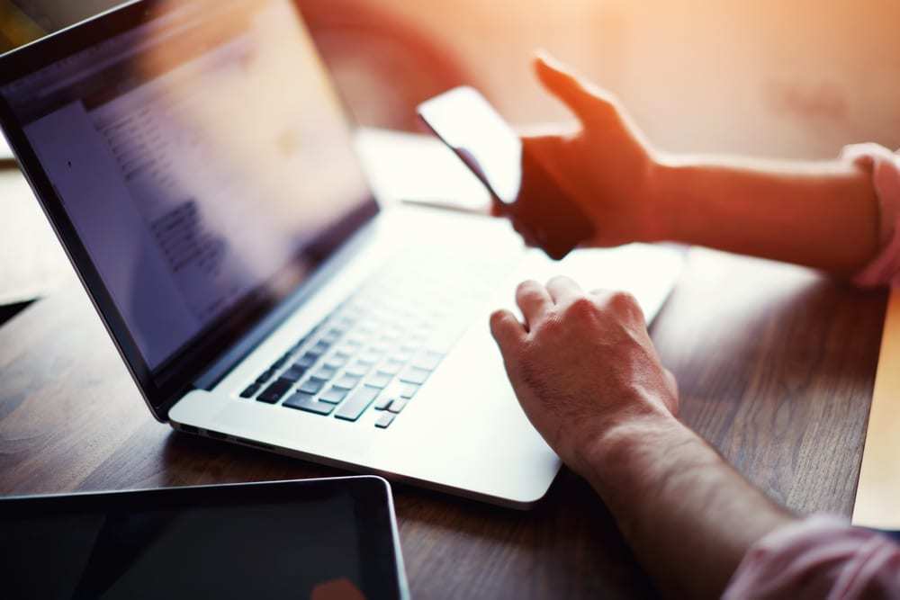 Man holding phone in front of open laptop