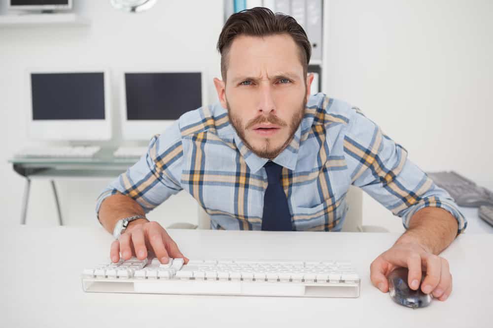 Young man in shirt and tie looking confusedly at computer