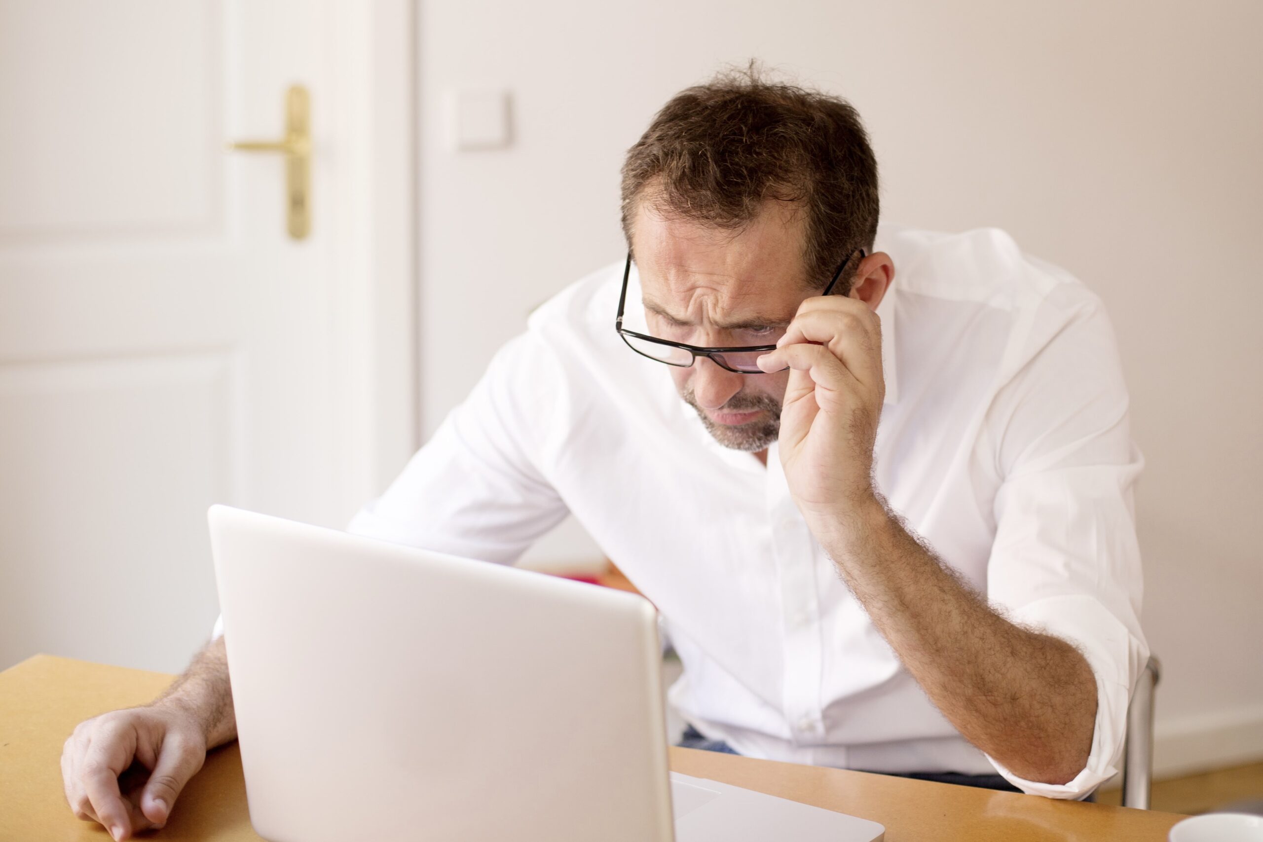 Man squinting at laptop, confused